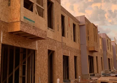 Close-up view of a row of townhouses under construction at sunset, showing exposed OSB sheathing
