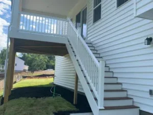 Finished exterior of a house with white horizontal siding and a new white-railed staircase leading up to an elevated back porch