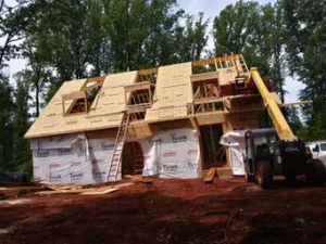 Front view of a house under construction with a gambrel roof, partially sheathed in OSB