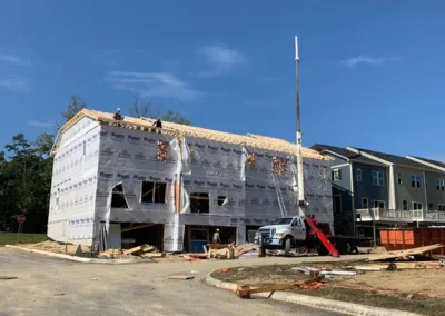 Residential building under construction, wrapped in white house wrap, with workers on the roof